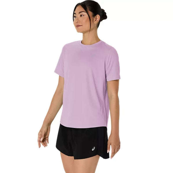 En kvinde står med ansigtet let vendt til siden og har en Asics Core Ss Top, Dame, i farven Hazy Lilac på samt sorte shorts med et lille hvidt logo på venstre ben, alt sammen på en ensfarvet hvid baggrund.