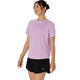 En kvinde står med ansigtet let vendt til siden og har en Asics Core Ss Top, Dame, i farven Hazy Lilac på samt sorte shorts med et lille hvidt logo på venstre ben, alt sammen på en ensfarvet hvid baggrund.