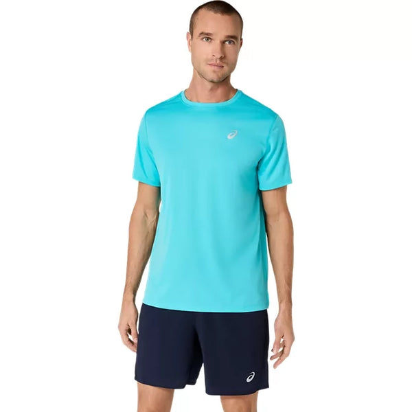 En mand står foran en ensfarvet hvid baggrund iført en Asics Core SS Top, Herre, Energy Aqua – en lyseblå løbetrøje til mænd – og mørkeblå shorts, hvor begge dele er forsynet med det lille Asics-logo.