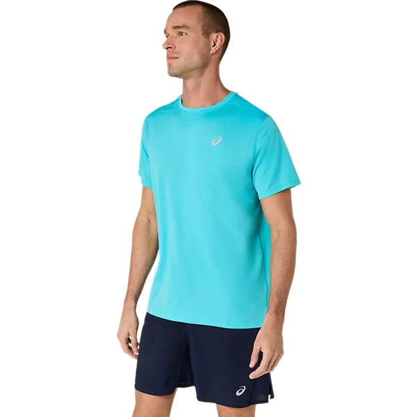 En mand står foran en ensfarvet hvid baggrund iført en Asics Core SS Top, Herre, i farven Energy Aqua og marineblå shorts, begge med små Asics-logoer.
