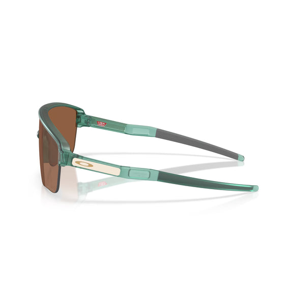 Et par Oakley Corridor SQ unisex udendørs sportsbriller med et gennemsigtigt grønt Trans Pacific-stel, Prizm Tungsten-linser, beige rektangulær accent på tindingen, "USA"-klistermærke på indersiden af armen og gråt gummigreb ved spidsen.
