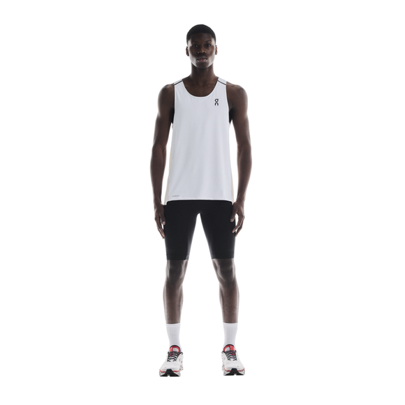 En herre står og kigger fremad iført On Performance Tank, Herre, White/Silver med sorte, tætsiddende shorts, hvide sokker og hvide løbesko med røde og sorte detaljer på en almindelig hvid baggrund.