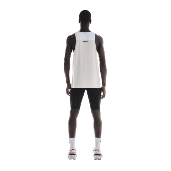 En person står med ansigtet vendt mod kameraet iført On Performance Tank, Herre, White/Silver, sorte shorts, hvide sokker og hvide sportssko med pink detaljer på en almindelig hvid baggrund.