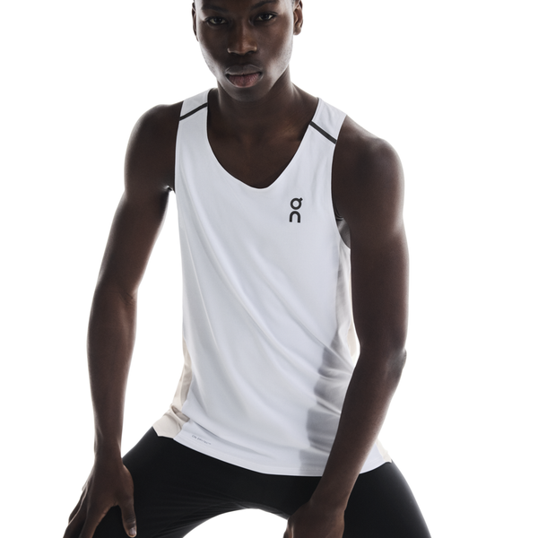En mand i On Performance Tank, Herre, White/Silver med et diskret sort logo står på en hvid baggrund og læner sig frem med hænderne på benene - klar til intens løbetræning.