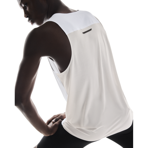 En person bærer On Performance Tank, Herre, White/Silver og sorte leggings, mens hun strækker sig mod en hvid baggrund - perfekt til løbetræning eller enhver aktiv herre.