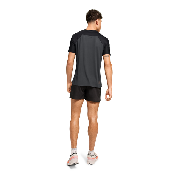 En mand kigger væk og er iført On Performance-T, Herre, Black/Eclipse med sorte shorts og hvide sneakers med orange detaljer på en almindelig hvid baggrund.
