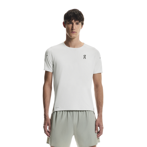 En mand med kort brunt hår står med front mod en hvid baggrund iført On Performance-T, Herre, Iceberg/Tin t-shirt med et lille sort logo og lysegrå shorts - en ideel åndbar trænings t-shirt.