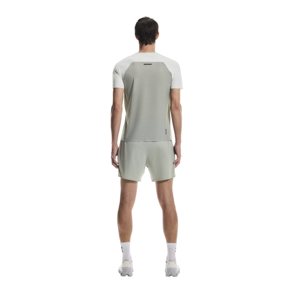 En mand ser væk fra kameraet og er iført On Performance-T, Herre, Iceberg/Tin med matchende shorts, hvide sokker og hvide sneakers på en almindelig hvid baggrund.