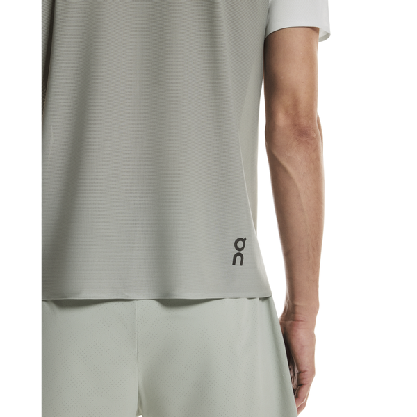 En person ses bagfra iført On Performance-T, Herre, Iceberg/Tin-an åndbar trænings t-shirt med matchende shorts. Kun højre arm plus dele af overkroppen og benene er synlige.