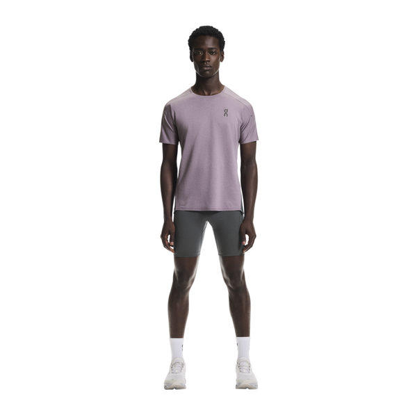 En mand står og kigger fremad iført On Performance-T til mænd i Dewberry/Eclipse, grå, tætsiddende shorts, hvide strømper og hvide sneakers på en almindelig hvid baggrund.