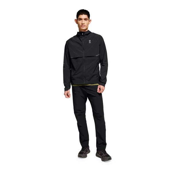 En mand står med ansigtet fremad i On Core Jacket, Herre, Black, sammen med sorte bukser og sorte sportssko. Tøjet har minimal branding, og baggrunden er helt hvid.