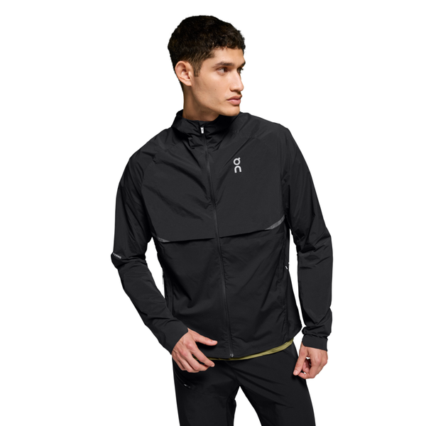 En mand iført On Core Jacket, Herre, Black og sorte bukser står på en hvid baggrund og kigger til venstre med den ene hånd let strakt frem.