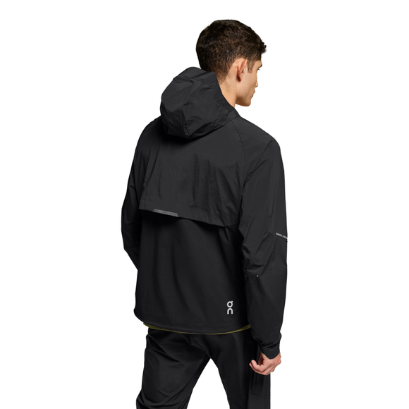 En mand ses bagfra iført On Core Jacket, Herre, Black med matchende sorte bukser. Den vandafvisende jakke har en ventileret flap, et lille hvidt logo nederst på ryggen, reflekterende detaljer og en hvid baggrund.