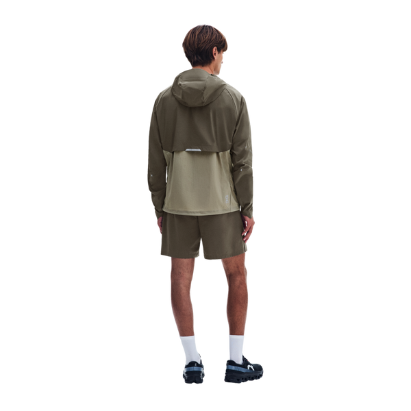 Bagfra-billede af en person iført en On Core-jakke, Herre, i farven Bark/Vetiver med et lysere grønt nederste panel, matchende shorts, hvide sokker og mørke sportssko.