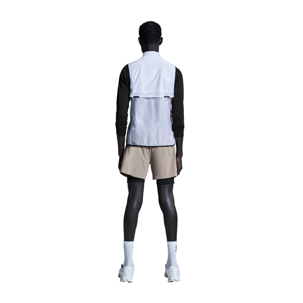 En person vender ansigtet væk og er iført en hvid vest over en sort langærmet skjorte, On 5" Performance 2/1 Shorts til mænd i Cinder/Black, hvide strømper og hvide sportssko på en almindelig hvid baggrund.