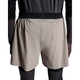 En person i sort langærmet sportstøj og beige 5" Performance 2/1 Shorts, Herre, Cinder/Black from On står med ryggen til. Shortsene har hurtigtørrende materiale og "SWISS ENGINEERING" på linningen.