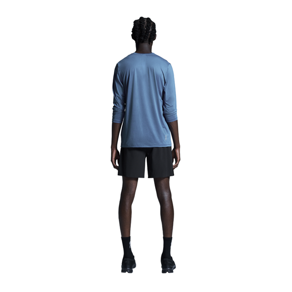 En person står med ryggen til kameraet og er iført en blå langærmet skjorte og et par ON 7 Performance Shorts, Herre, Sort – perfekte letvægts løbeshorts til enhver aktivitet. Sorte sokker og sorte sneakers fuldender looket, der fremstår på en ensfarvet hvid baggrund. Personens arme hænger naturligt ned langs siden.