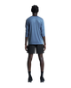 En person står med ryggen til kameraet og er iført en blå langærmet skjorte og et par ON 7 Performance Shorts, Herre, Sort – perfekte letvægts løbeshorts til enhver aktivitet. Sorte sokker og sorte sneakers fuldender looket, der fremstår på en ensfarvet hvid baggrund. Personens arme hænger naturligt ned langs siden.