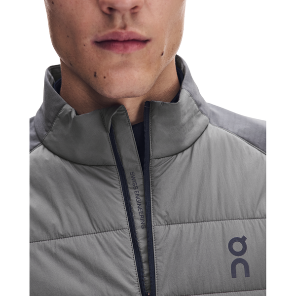 Nærbillede af en person iført en Eclipse/Ember On Weather Hybrid-jakke, Herre, der er udført i et gråt, vind- og vandafvisende, isoleret design med krave med lynlås og et logo på brystet.