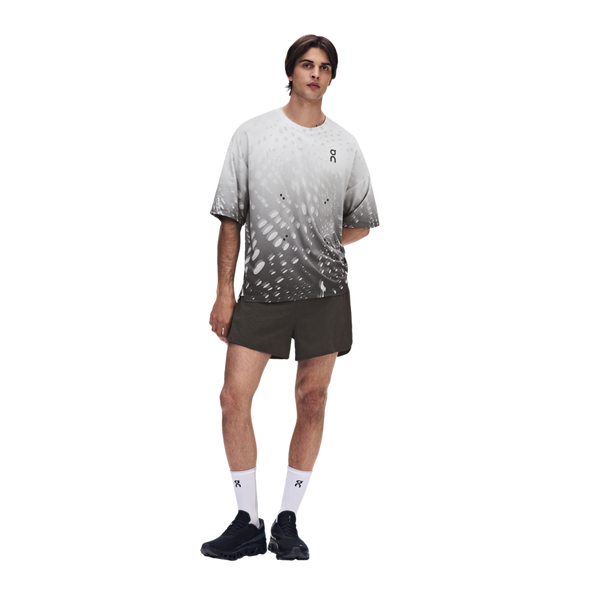 En mand står foran en hvid baggrund iført en grå og hvid T-shirt med farveovergang, ON Performance Volt Shorts Herre Espresso, hvide sokker med et lille logo og sorte sportssko. Den ene arm har han bag ryggen.