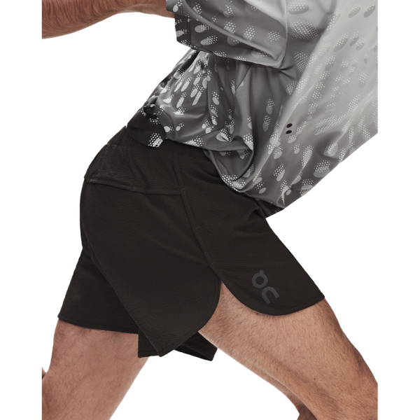 En person iført en mønstret grå sportstrøje og ON Performance Volt-shorts i farven Herre, Espresso strækker sig fremad og fremhæver dermed komforten ved disse ON-shorts.