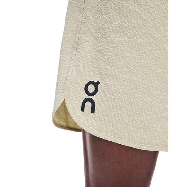 Nærbillede af den nederste del af ON Performance Volt Shorts, Herre, Hare i lys beige med et lille sort ON-logo i nederkanten, båret af en person med mørk hud.