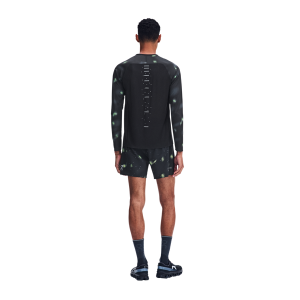 Bagfra-billede af en person iført en langærmet sportstrøje og Performance Shorts Lumos, Herre, Sort, begge med et sort mønster og grønne, lyslignende detaljer, kombineret med mørke strømper med rund kant og løbesko.
