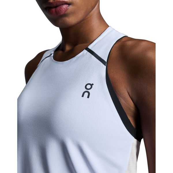 Nærbillede af en kvinde iført On Performance Tank, Dame, White/Silver med et lille sort logo på brystet. Hendes ansigt er delvist synligt mod en hvid baggrund.
