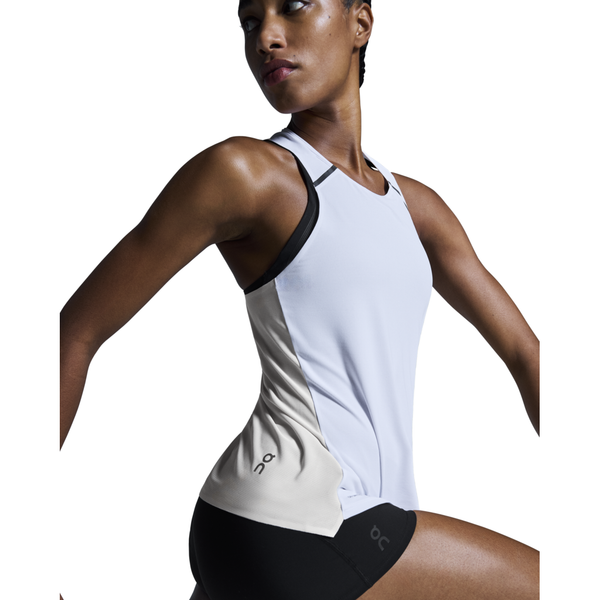 En kvinde iført On Performance Tank, Dame i hvid/sølv og matchende sorte shorts poserer på en hvid baggrund.
