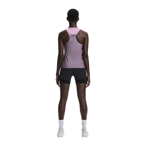 En person vender sig væk fra kameraet iført en On Performance Tank, Dame, Sakura/Dewberry, med sorte shorts og hvide sko - og fremhæver åndbar løbetøj mod en almindelig hvid baggrund.