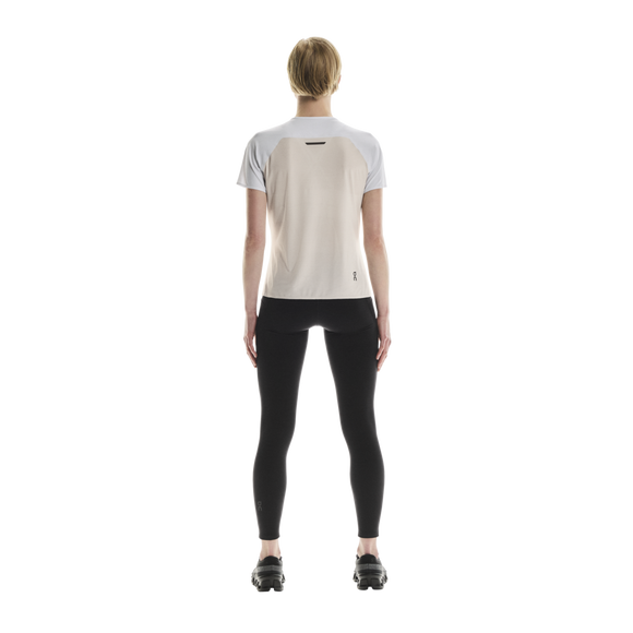 En person står med ryggen til kameraet iført en ON Performance-T, Dame, hvid/sølv, kombineret med sorte leggings og sorte sportssko foran en ensfarvet hvid baggrund.
