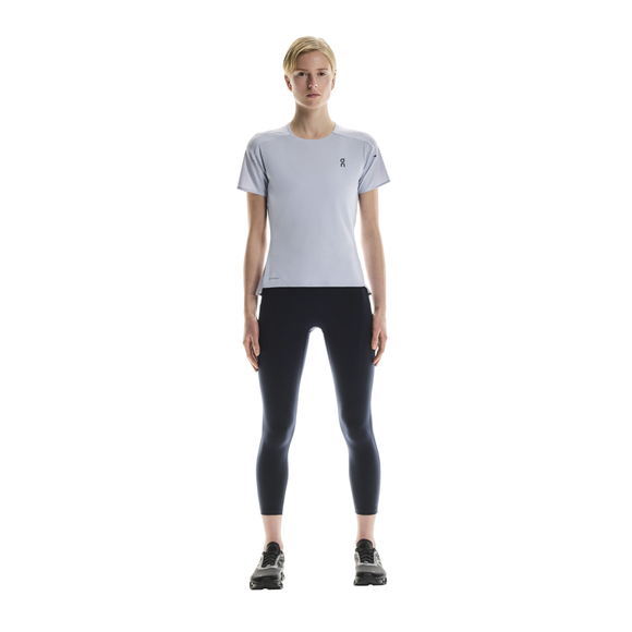 En kvinde står med ansigtet fremad og er iført On Performance-T Dame i Nimbus/Lilac, mørke leggings og sorte sportssko på en almindelig hvid baggrund.