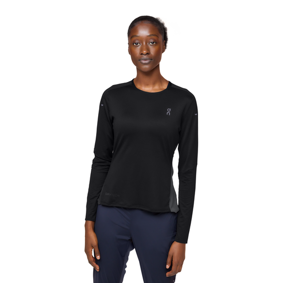 En person ser frem for sig iført On's Performance Long-T, Dame, Black/Eclipse med et lille hvidt logo på brystet og marineblå træningstøj dame-bukser på en almindelig hvid baggrund.