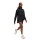 En person iført en On Core Jacket, Dame, i sort, sammen med sorte shorts og hvide sneakers, går frem mod en almindelig hvid baggrund.