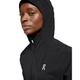 En kvinde iført On Core Jacket, Dame, Black med et lille hvidt logo på brystet, kigger lidt til siden mod en almindelig hvid baggrund.