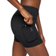 En kvinde iført On Performance Tights Short, Dame, Black stikker en smartphone ned i sidelommen og understreger shortsens praktiske design og anvendelighed til en aktiv livsstil.