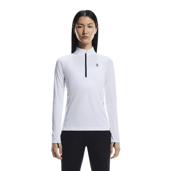 En kvinde med langt, glat sort hår ser frem for sig iført On Climate Shirt, Dame in White og sorte leggings på en almindelig hvid baggrund.