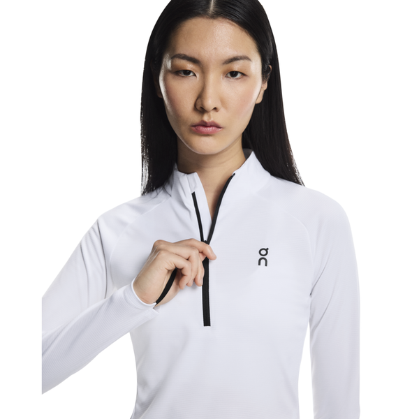 En kvinde med langt glat hår bærer On Climate Shirt, Dame, White, uden lynlås foroven. Den almindelige hvide baggrund får logoet på venstre bryst til at skille sig ud.