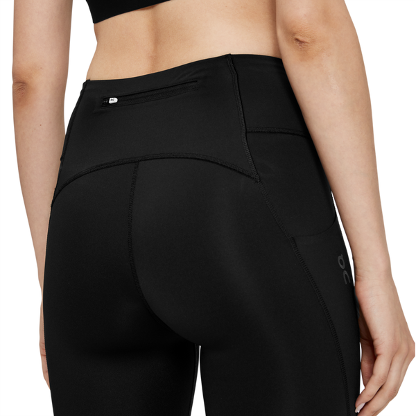 Nærbillede af en person iført On Performance Tights Short, Dame, Black, der fremhæver den bageste linning med en lille lynlåslomme og mærkets logo, der er synligt på siden.