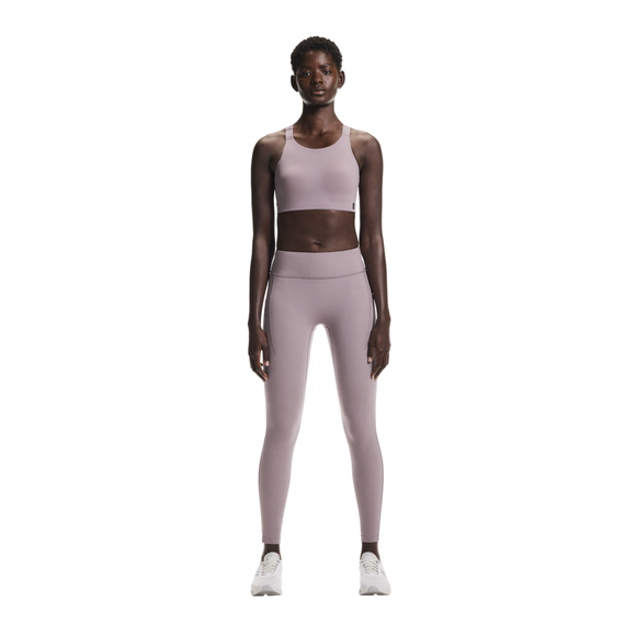 En kvinde kigger fremad i On's Performance Tights, Dame, Heron, sammen med en sports-bh og hvide sneakers på en almindelig hvid baggrund.