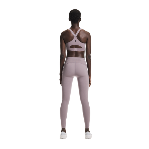 En kvinde kigger væk fra kameraet iført On Performance Tights, Dame, Heron og en matchende racerback sports-bh med udskæringsdetaljer - perfekte løbetights dame - sammen med hvide sportssko.