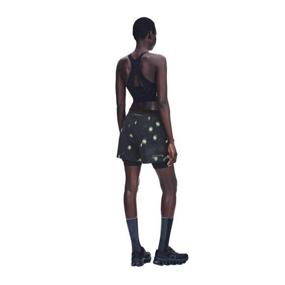 En kvinde set bagfra iført en sort sports-BH med racerryg og sorte Performance Shorts Lumos, Dame, med et lysegrønt cirkulært mønster.