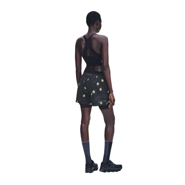 En kvinde set bagfra iført en sort sports-BH med racerryg og sorte Performance Shorts Lumos, Dame, med et lysegrønt cirkulært mønster.