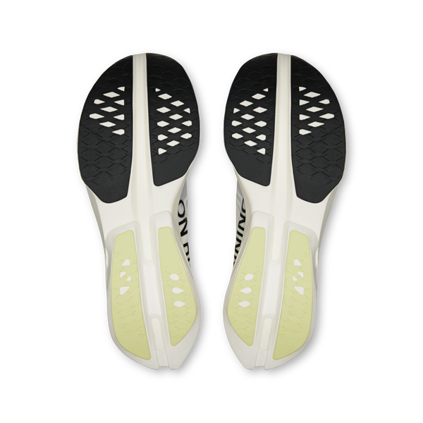 Et par On Cloudboom Strike konkurrencesko til mænd i Juniper/Limelight, vist fra bunden med sort og lysegul tekstureret gummiydersål og udskårne mønstre for forbedret greb og støtte mod en hovedsageligt hvid base.
