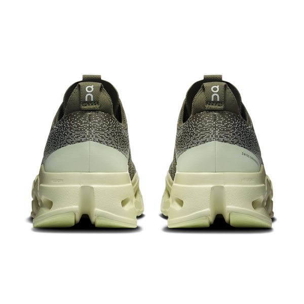 On Cloudsurfer Max herre løbesko i Olive/Seedling er vist bagfra på en hvid baggrund og har tykke CloudTec Phase-såler og "On"-branding på hver hælkappe for optimal komfort.