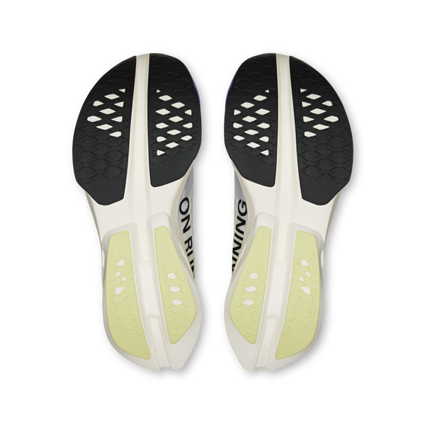 Et billede oppefra og ned af ydersålerne på On Cloudboom Strike Dame løbesko i Juniper/Limelight med sorte, hvide og gule detaljer med diamantformede udskæringer på gummislidbanen.