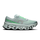 En ON Cloudmonster 3 løbesko til kvinder i farven Ivory/Topaz har en overdel i mesh, grå snørebånd, grøn ON RUNNING-tekst og en tyk hvid sål med CloudTec-støddæmpning og udskårne detaljer. Vist på en ensfarvet hvid baggrund.