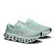 ON Cloudmonster 3 Dame i farvekombinationen Ivory/Topaz har CloudTec-støddæmpning, perforerede såler, hvide snørebånd og grønne detaljer med teksten »ON RUNNING« i grønt på hælen, vist på en ensfarvet hvid baggrund.