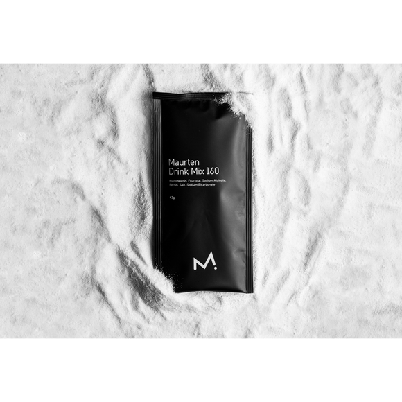 En sort Maurten Drink Mix 160-pakke med et hvidt M-logo hviler på en hvid, pulveragtig overflade, der viser produktets ingredienser og fremhæver denne innovative energidrik.