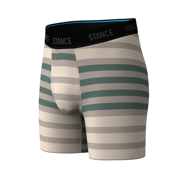 Stance Double Stripe Wholester herre-boxershorts i croissant-stil har vandrette grønne og beige striber og er fremstillet af Butter Blend-stof i høj kvalitet, der sikrer enestående blødhed. Disse komfortable herre-boxershorts er designet med en tætsiddende pasform og et sort elastisk linning med STANCE-logoet i hvidt og præsenteres her på en ensfarvet hvid baggrund.